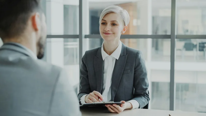 A recruiter interviewing a candidate across a table with a clipboard, for a hiring workflow.